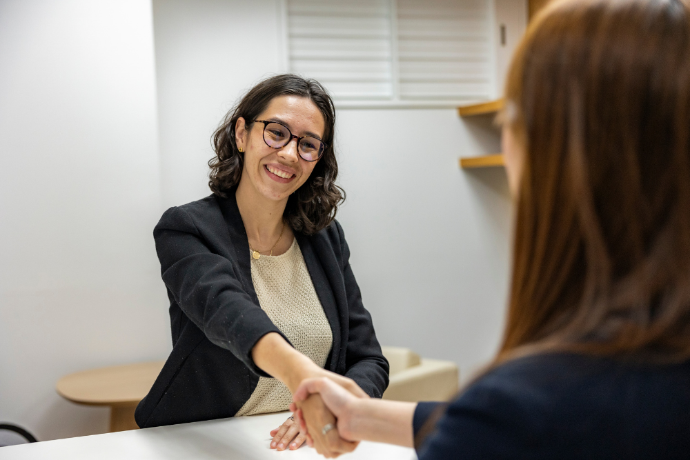 two female professionals shaking hands with one of the women smiling